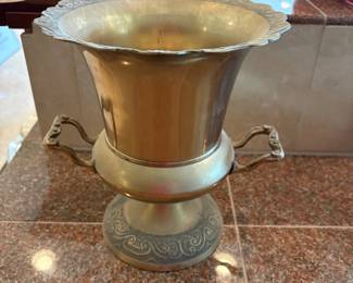lp- This elegant brass champagne bucket measures approximately 9 inches by 9 inches, featuring a flared rim with intricate scrollwork detailing around the edge. The bucket is supported by a sturdy base adorned with ornate matching patterns, adding a classic and sophisticated touch. Two gracefully curved handles provide ease of use while complementing the vintage aesthetic. Perfect for chilling champagne or as a decorative centerpiece, this brass bucket combines functionality with timeless design.