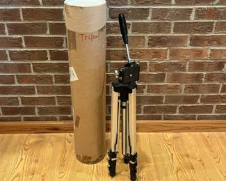 im- This Manon #800 tripod is a sturdy and adjustable support designed for cameras and other equipment. Crafted from lightweight aluminum, it features extendable legs with secure locks and a smooth, easy-to-operate pan-and-tilt head with a comfortable handle. The tripod folds compactly for portability and comes with a tall cylindrical carrying tube for safe storage and transport. Its silver metallic finish combined with black hardware highlights a professional and durable design suitable for photographers and videographers alike. H: 24in