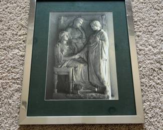 dr- Framed art print featuring a classical Greco-Roman style stone relief depicting three figures, with one seated figure flanked by two standing figures in draped garments. The detailed monochromatic image captures the sculptural texture and form of an ancient-style carved relief. Presented under glass with a dark green mat and silver-tone metal frame. The reverse retains an older board backing with hanging wire. No visible artist signature, title, date, or identifying information was found, and the specific relief depicted is unknown. Attractive decorative piece well suited for a classical art, antiquities, architectural, or traditional décor collection.