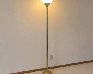iq- This torchiere floor lamp features a classic design with a brass finish, providing a warm and inviting glow to any room. The lamp includes a frosted glass shade that diffuses light softly upwards, creating ambient lighting ideal for living rooms or reading corners. Its tall, slender metal body stands steadily on a round brass base with decorative edging. The lamp is equipped with a convenient side knob switch for easy operation. Its elegant gold tones and clean lines make it a versatile addition to both modern and traditional interiors.