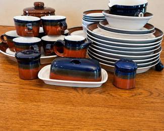 ew- This complete Mikasa Potters Art dinnerware set, designed by Ben Seibel and made in Japan, features the distinctive Fire Song pattern. The set includes various plates, cups, saucers, and serving pieces all showcasing a rich brown and navy color scheme accented with white interiors. Crafted from durable pottery, this stoneware collection combines functional design with artistic flair, making it a standout addition to any table setting or collector's showcase.
