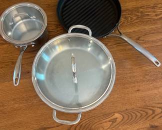 iu- This Calphalon 3-piece cookware set features a durable stainless steel saucepan, a grill pan with ribbed non-stick surface, and a large sauté pan with a tempered glass lid. Highlighted by its sleek, brushed metal handles and black non-stick interior, the grill pan measures approximately 12 inches in diameter for versatile stovetop grilling. Each piece is constructed from high-quality materials designed for even heating and long-lasting performance, perfect for everyday cooking and grilling needs.