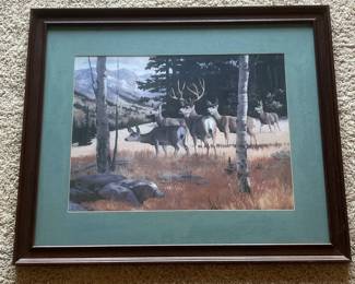 db- This beautifully framed wildlife art print showcases a serene scene of five deer standing in a grassy meadow with a backdrop of trees and distant mountains. The print is set within a classic dark wood frame that features subtle carved details and a rich brown finish. A muted green mat surrounds the artwork, enhancing the natural tones and drawing the eye to the detailed depiction of the deer. The back of the frame includes a wire hanger for easy wall mounting. Ideal for nature enthusiasts and those looking to add a touch of rustic charm to their decor.