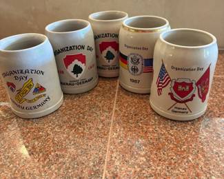 lo- This collection features 5 vintage beer steins commemorating 'Organization Day' events held by United States Army units stationed in Hanau, Germany. Each stein is crafted from sturdy ceramic material with a traditional stein shape, showcasing detailed military insignias and colorful unit crests. Highlighting the 23rd Engineer Battalion, these steins are decorated with vibrant red, green, black, and gold accents, including a distinctive gold rim around the top. The front displays the unit insignia and event details, while the back features the combined flags of the United States and Germany along with the year 1987. These collectible steins capture a unique piece of military history and heritage.