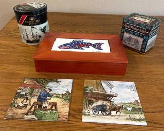 lb- This unique collection of various collectors' items includes a wooden box with a colorful fish design, two vintage-style decorative tins with intricate artwork, and two detailed trivets depicting rural scenes. The wooden box is crafted from warm-toned wood with a vibrant fish illustration on the lid, adding a splash of color. The tins feature ornate, classic designs—one with floral patterns and German-style imagery, and the other adorned with black and white nautical graphics. The coasters showcase picturesque countryside scenes in soft, earthy tones, highlighting historical charm and artisanal quality. Each piece combines distinctive aesthetics and materials, ideal for collectors or decorative displays.