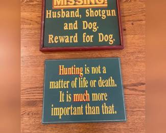 fw- This Hunters Wall Art set features two unique decorative signs with witty hunting-themed sayings. The first sign, framed in dark wood, reads 'MISSING! Husband, Shotgun and Dog, Reward for Dog,' adding a playful touch to any hunter's space. The second sign carries the statement 'Hunting is not a matter of life or death. It is much more important than that,' emphasizing a humorous passion for hunting. Both signs showcase bold yellow and orange text on a dark green background, measuring approximately the size of a small plaque, perfect for indoor wall display.