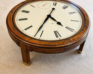 hb- This unique coffee table features a working Howard Miller clock integrated into a solid oak frame. The table stands 16 inches tall and has a 41.5-inch round top, showcasing an elegant clock face with Roman numerals and a small seconds dial. The rich oak wood and brass-capped legs add classic appeal, making it both a functional timepiece and a striking piece of furniture.