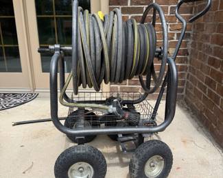 ib- This portable hose caddy features a robust metal frame with sturdy wheels for easy maneuverability. It includes a long black hose neatly coiled on the reel and a durable spray nozzle with multiple settings. The hose caddy is designed for convenient outdoor use, providing efficient water distribution and storage. Its compact size and handle make it easy to transport and store when not in use.