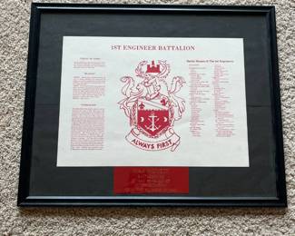 cb- This framed commemorative plaque honors the 1st Engineer Battalion, featuring the battalion's crest prominently in red and white with the motto 'Always First.' It includes detailed battalion history, battle honors, and three inscriptions: 'Grant of Arms,' 'Blazon',' and 'Symbolism.' The plaque features a personalized dedication to Major Wonsik, Battalion XO, marking service from 27 May 1986 to 8 June 1987, presented in appreciation from the soldiers of HHC. The item is displayed in a black frame with a matte black background, highlighting the red engraving plate. The plaque's dimensions and the frame's condition, including close-up views of the frame corners, indicate a well-preserved collectible military memorabilia piece.