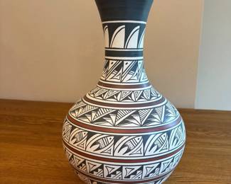ay- This exquisite 15-inch tall and 10-inch wide ceramic vase is a fine example of Native American artistry, hand crafted and hand painted by Navajo artist Nelson Maloney. The vase features traditional black and white geometric patterns with intricate detailing and a subtle reddish-brown accent line encircling the body. Its unique shapes and motifs reflect the cultural heritage and skilled craftsmanship of the Navajo people. Perfect for collectors and enthusiasts of Native American pottery, this piece combines artistry with cultural significance.