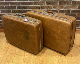 in- This vintage suitcase set features two sturdy hard shell suitcases in a rich, warm brown color with a textured finish. The cases are accented with shiny chrome hardware, including a robust locking mechanism, metal trim, and comfortable leather-wrapped handles. Inside, both suitcases are lined with cream-colored fabric; the larger case includes elastic sections for secure packing, while the smaller case features structured compartments. The one showcases the distinctive 'Escort' logo and has a classic mid-century style while the other is sporting the "American Tourister" logo, making them a stylish and functional choice for collectors or travelers seeking a retro aesthetic.