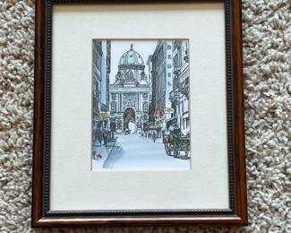 en- This framed art captures a detailed architectural street scene, featuring a prominent domed building in the background. The artwork highlights fine line work and subtle color accents that bring the cityscape to life. The piece is set within a dark wood frame with intricate beaded detailing along the inner edge, complemented by a cream-colored mat that provides an elegant contrast. The back of the frame includes a sturdy hanging wire and a gallery label from Framing Avenue in Downers Grove, IL, indicating professional framing craftsmanship.