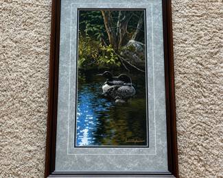 dc- Framed wildlife art print titled “Dancing Water – Loons” by Persis Clayton Weirs, depicting a pair of common loons floating on a quiet woodland pond. The vertical composition features finely detailed birds, reflective water, and a shaded forest background. The print is signed by Persis Clayton Weirs in the lower right. According to the accompanying Wild Wings Collection Certificate of Authenticity, the work was reproduced in 1994 from the artist’s original painting on pH-neutral archival paper using fade-resistant inks. It is identified as a signature limited open edition, which included 100 artist proofs. Each print was personally inspected and signed by the artist. Professionally framed by Wild Wings with coordinating matting and a dark wood-tone frame. Includes the original Certificate of Authenticity and artist biography paperwork shown. The published image size is approximately 9” x 19”