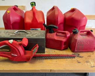 mo- This comprehensive outdoor trimmer set includes a red electric Homelite trimmer, multiple red gas cans in various sizes, and a sturdy metal toolbox. The trimmer is compact and lightweight, designed for easy handling. The gas cans, made of durable plastic, feature ergonomic handles for convenient pouring and storage. The metal toolbox provides ample storage space for trimmer accessories and tools, showcasing a well-used but solid construction. This set is ideal for maintaining your garden and outdoor spaces efficiently.