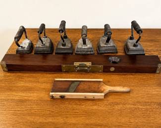 fz- This unique collection features six small antique irons, each with a distinct handle design, crafted from metal and showing natural patina and wear indicative of their age. Included is a vintage level made of rich dark wood and a wooden-handled mandolin accessory with a metal blade element. The set is an excellent example of early domestic tools, ideal for collectors interested in vintage household items or decorative rustic accents.