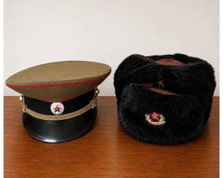 ak- Pair of vintage Soviet military headgear dating to the late Cold War era, including an olive drab officer-style visor cap and black fur winter ushanka. The visor cap features an olive crown with red piping, black band and visor, gold braided chin cord, and Soviet red star with hammer-and-sickle cockade. Interior is marked “ЦЭПК Москва” (Moscow) and size 57. The black fur ushanka features folding ear flaps and a Soviet red star with hammer-and-sickle insignia set within a gold-colored wreath. Interior retains a legible size/manufacturing label. Provenance: These hats were acquired in Germany around 1989 by the current owner, who was serving as a U.S. Army battalion commander at the time. They were purchased during the historic period surrounding the fall of the Berlin Wall and have remained in the owner’s possession since.