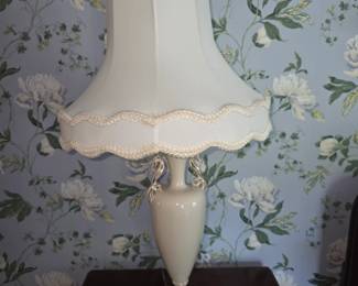vintage urn-style table lamp features an off-white ceramic body on a brass-accented base paired with a scalloped bell lampshade.    