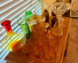 assortment of vintage and decorative glassware, including amber glass tumblers, pitchers, decanters, covered candy dishes, pressed-glass serving pieces, and more. Multiple pieces and colors available throughout the sale.