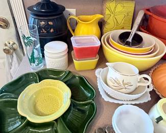Colorful vintage kitchenware featuring Tupperware containers, nesting mixing bowls, a yellow pitcher, butter crock, teacups, and a large leaf-shaped divided serving tray! 🍋✨
