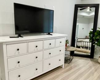 white dresser, tv, floor mirror, and wire basket