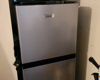  compact stainless steel refrigerator with a black microwave placed on top