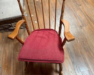 Wooden Spindle-Back Rocking Chair with Upholstered Seat Traditional wooden rocking chair featuring a spindle back, turned supports, curved armrests and warm wood finish. Includes a burgundy/red upholstered seat cushion. Classic design suitable for a living room, bedroom, nursery or reading area. Pre-owned condition with normal wear from use; see photos for details.