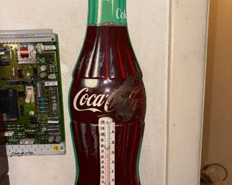 Metal advertising thermometer shaped like a Coca-Cola bottle, script logo, likely 1950s-60s style.