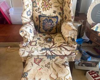 Crewel-Embroidered Wingback Chair with Ottoman:  Vintage wingback armchair and matching ottoman upholstered in cream Jacobean-style crewel-embroidered floral fabric, with a coordinating navy needlepoint accent pillow; same set shown from front and close-up of ottoman