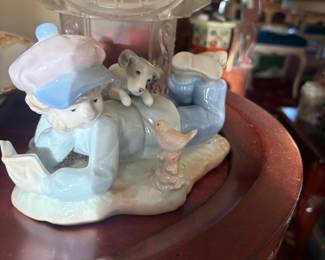 Porcelain boy reading with dog & bird figurine (Lladro/Nao style):  Glossy pastel-blue porcelain figurine of a boy in a beret lying on his stomach reading a book, with a small dog draped over his back and a bird perched nearby.