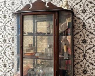 Victorian-style bow-front wall curio cabinet with curved glass: Wall-mounted display cabinet, shaped wood crest, curved (bow-front) glass sides and door, wood shelving inside.