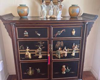 Chinese black lacquer cabinet with figural bone/shell inlay:  Two-door Chinese black lacquered cabinet with gilt-line decoration and applied carved bone/shell inlay depicting court figures, vases, and foliage; brass hardware with tasseled pull.