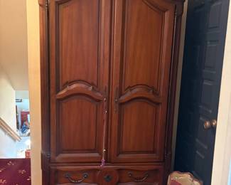 French Provincial-style cherry/mahogany armoire: Tall two-door bonnet-top armoire with arched raised panel doors, turned finials, two lower drawers with brass floral pulls, cabriole feet; likely a mid-late 20th