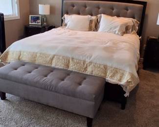 upholstered button-tufted bed with a curved dark wood frame and a matching grey tufted storage bench