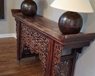 The image shows an antique Chinese wooden altar table with intricate hand-carved fretwork along the apron and sides, styled with two sphere-based table lamps on top