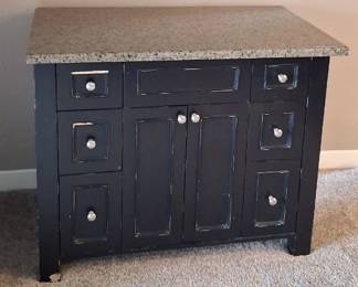 black bathroom vanity with a speckled stone top and six side drawers.