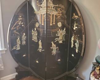 This is an Oriental Furniture 6-foot tall black lacquer round room divider featuring intricate hand-carved mother-of-pearl inlay depicting traditional royal figures and a pavilion scene.