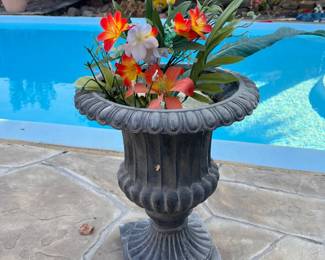Classic dark gray resin garden urn with a fluted design and square base. This planter contains a variety of colorful artificial flowers including orange, red, and white lilies with green foliage.
