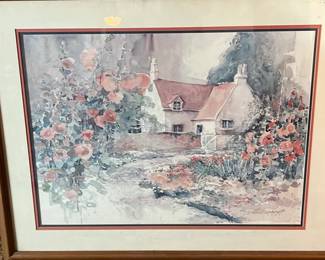 Framed watercolor painting "The Garden House" depicts a quaint cottage surrounded by blooming pink flowers. The artwork is set within a multi-layered mat and a wooden frame. The piece is signed by the artist Dawna/Dalina Barton (1986), in the lower right corner.