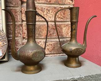 Vintage brass ewer (aftaba) set. Brass pitchers with intricate hand-etched floral designs. This set includes two vessels of varying heights, each with a long curved spout and a decorative handle. The brass has a natural aged patina and one pitcher includes a removable lid.
