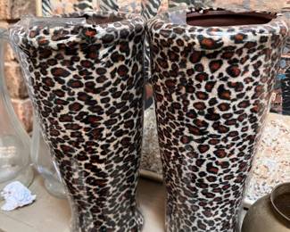 Stylish pair of ceramic vases with a leopard print fabric wrap. These vases have a brown interior and a tapered cylindrical shape. The leopard pattern is a classic brown, black, and tan color scheme. One vase has a small broken piece inside that is not visible from the exterior. Both items are still in their original cellophane wrap.  Note: Discounted... One vase was accidentally dropped and has a broken piece on the inside near the top. 