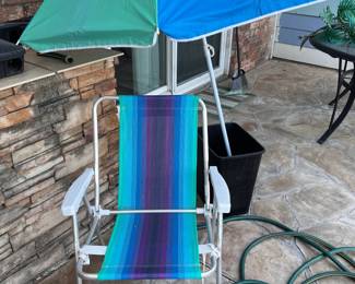 Folding Beach Chair & Umbrella. Colorful folding beach chair and matching umbrella set. The chair has a lightweight aluminum frame with a striped blue, purple, and green fabric seat. The umbrella is blue and green with a white pole and a tilt mechanism.