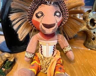 Authentic Disney The Lion King Broadway Musical Simba plush is made of soft fabric with a synthetic fiber mane. This collectible doll has a brown, orange, and yellow color scheme with intricate patterns on the clothing and headpiece. It is a licensed Walt Disney Theatrical product.