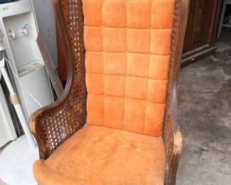 Vintage wingback chair has orange tufted velvet upholstery and dark wood framing. The side panels are constructed with woven cane. The chair features a high back with a tufted pattern and curved wooden arms.