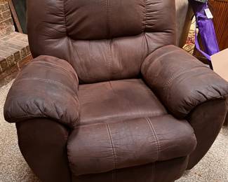 Comfortable Ashley Furniture McGann Manual Rocker Recliner chair is upholstered in brown faux leather. This piece has contrast white stitching and padded armrests. The seat and backrest are cushioned for support.  Estimated (WxDxH): 38 x 36 x 40 in