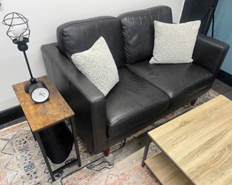 One of five matching modern black leather loveseats; one of many matching modern industrial-style coffee tables; one of nine matching narrow end tables with black fabric magazine sling.
