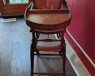 Antique Victorian-Style Convertible Child’s High Chair  Antique wooden convertible child’s high chair featuring an ornate carved crest, caned seat and backrest, removable wooden feeding tray, turned stretchers, footrest, small metal wheels, and a mechanical folding/adjusting frame. The chair appears designed to convert or reposition for use as a high chair and low rolling chair.  This piece has significant age-related wear and damage, including broken and missing sections of the decorative crest, damaged or weakened cane weaving, finish loss, scratches, scuffs, loose or exposed hardware, and possible missing components. The adjustment mechanism has not been tested.  For decorative display, restoration, or collection only—this antique chair does not meet modern child-safety standards and should not be used by a child. Sold as-is; please review all photographs carefully. Rest well tonight, Teresa—we got through quite a collection! 