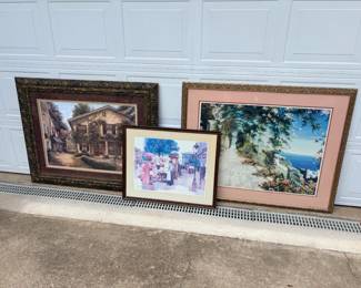 This lot includes three framed prints: a garden and stone building scene in an ornate gold-toned frame, a coastal cliffside view with a mauve mat in a carved gold frame, and a smaller street market or garden scene with figures in a gold frame. All are matted and framed under glass and ready to hang. A coordinated grouping for a hallway, stairwell, or gallery wall.