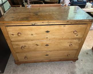 This pine chest features three graduated drawers with turned wood knobs and diamond-shaped dark escutcheons at each keyhole, set on bracket feet. A protective panel covers the top surface. The natural pine finish shows honest wear and knot character throughout — a solid, casual piece for a bedroom, entry, or hallway.