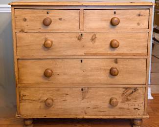 This pine chest has two short drawers over three long graduated drawers, each with turned wood knobs and dark keyhole escutcheons, standing on turned bun feet. The natural pine shows knots, grain variation, and honest surface wear consistent with age and use. A roomy, casual chest for a bedroom or entry.