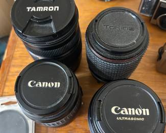 This camera lens lot includes a Tamron zoom lens, a Tokina zoom lens with red accent ring, two Canon EF lenses including a Canon Ultrasonic, a Canon PowerShot digital point-and-shoot, and a vintage 35mm film camera.